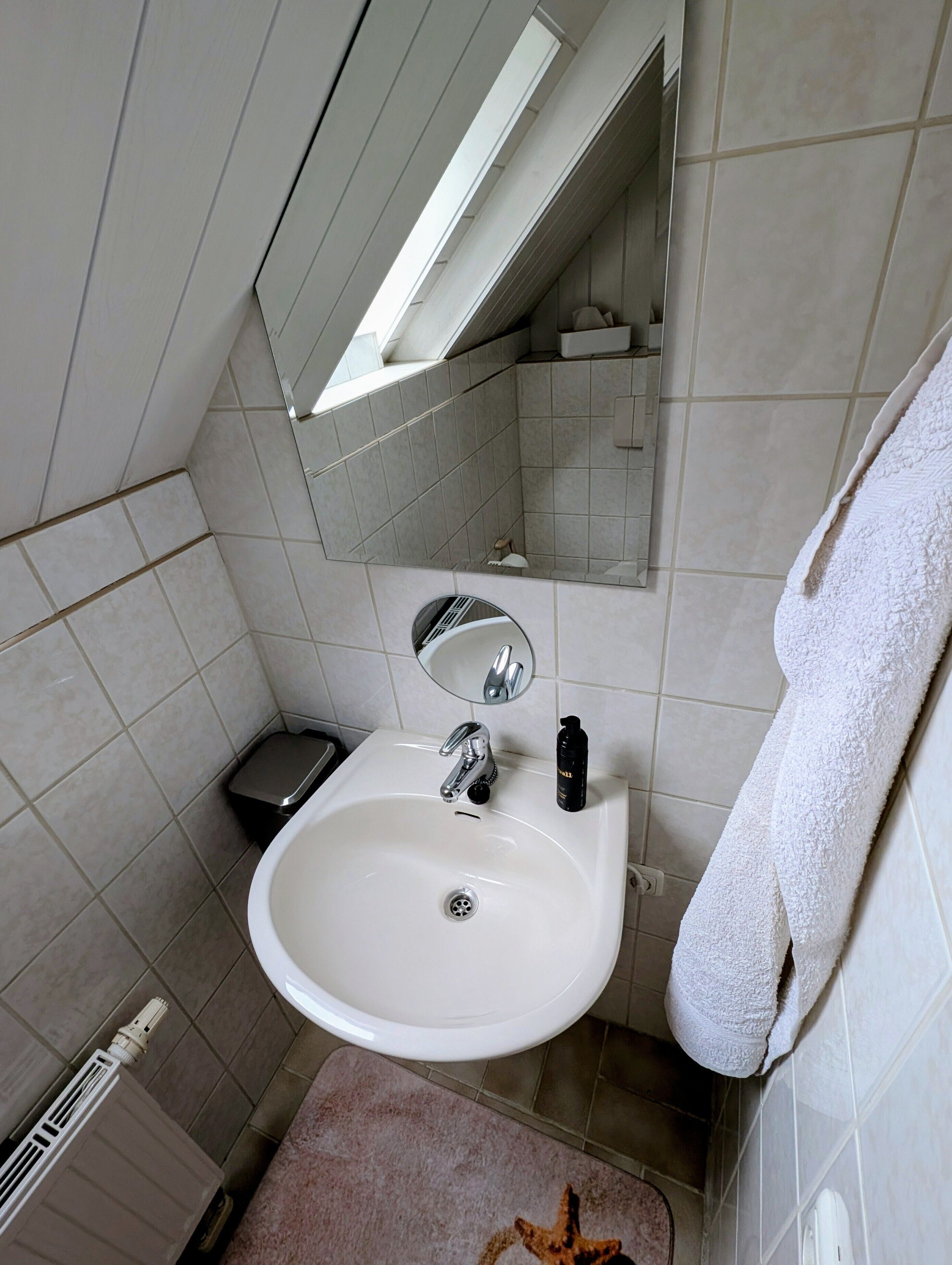 A bathroom with a white sink, a mirror, and a towel hanging on the wall.