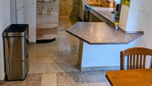 Een compacte keuken met een inbouwoven, een klein spoelgedeelte en een eethoek met een houten tafel en stoelen.