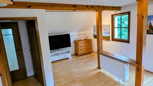 Een ruime kamer met houten balken, een televisie, een dressoir en een raam met uitzicht.
