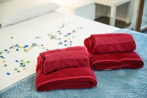 Un letto rifatto con un copriletto blu e due asciugamani rossi piegati sopra.