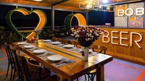 A restaurant interior with a long wooden table set for dining, a heart-shaped neon sign, and a 'BOB BEER' sign on the wall. - Cồn Phụng Retreats Mekong - Nature Island with Free Boat Shuttle & Fishing (Phu Tuc)