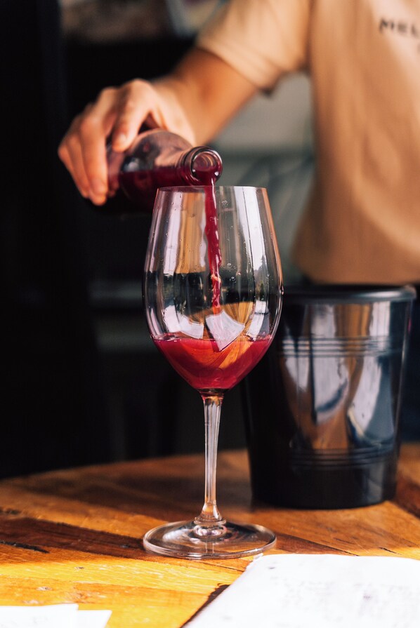 Una copa de vino tinto siendo servida, un cubo negro y una mesa de madera.