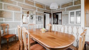 A dining area with a wooden table, six chairs, a fruit bowl, and a stone-patterned wall.