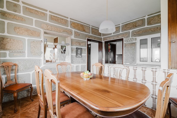 A dining area with a wooden table, six chairs, a fruit bowl, and a stone-patterned wall.