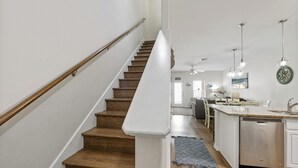 A modern kitchen with a wooden staircase, white cabinetry, and a built-in dishwasher. - 3 Heated Pools-Walk 2 Beach-Whitecap NPI (Corpus Christi)