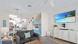 A modern living room with a sofa, coffee table, and a TV displaying a beach scene. - 3 Heated Pools-Walk 2 Beach-Whitecap NPI (Corpus Christi)