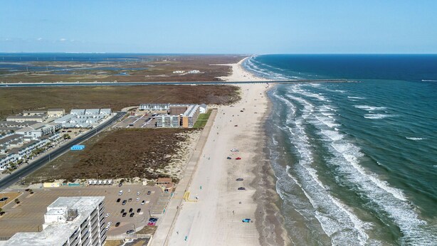 An aerial view of a coastal area with a beach, a parking lot, and buildings along the shore. - 3 Heated Pools-Walk 2 Beach-Whitecap NPI (Corpus Christi)