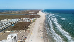 An aerial view of a coastal area with a beach, a parking lot, and buildings along the shore. - 3 Heated Pools-Walk 2 Beach-Whitecap NPI (Corpus Christi)