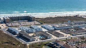 An aerial view of a coastal hotel with multiple buildings, a parking lot, and a beach in the background. - 3 Heated Pools-Walk 2 Beach-Whitecap NPI (Corpus Christi)