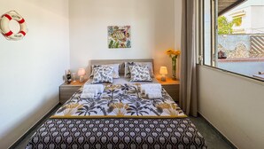 Un lit bien fait, recouvert d’une couvre-lit à motifs floraux, un gilet de sauvetage accroché au mur et un tableau au-dessus du lit.