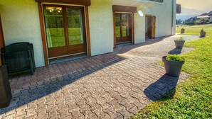 A modern building with a paved entrance, wooden doors, and a small outdoor seating area.