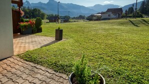 A grassy area with a paved walkway leading to a building entrance, surrounded by mountains and clear skies.