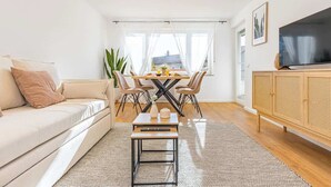 A modern living room with a sofa, a dining table with chairs, a coffee table, a TV, and a wooden cabinet. - SMS Homes I time out in Blaichach (Blaichach)