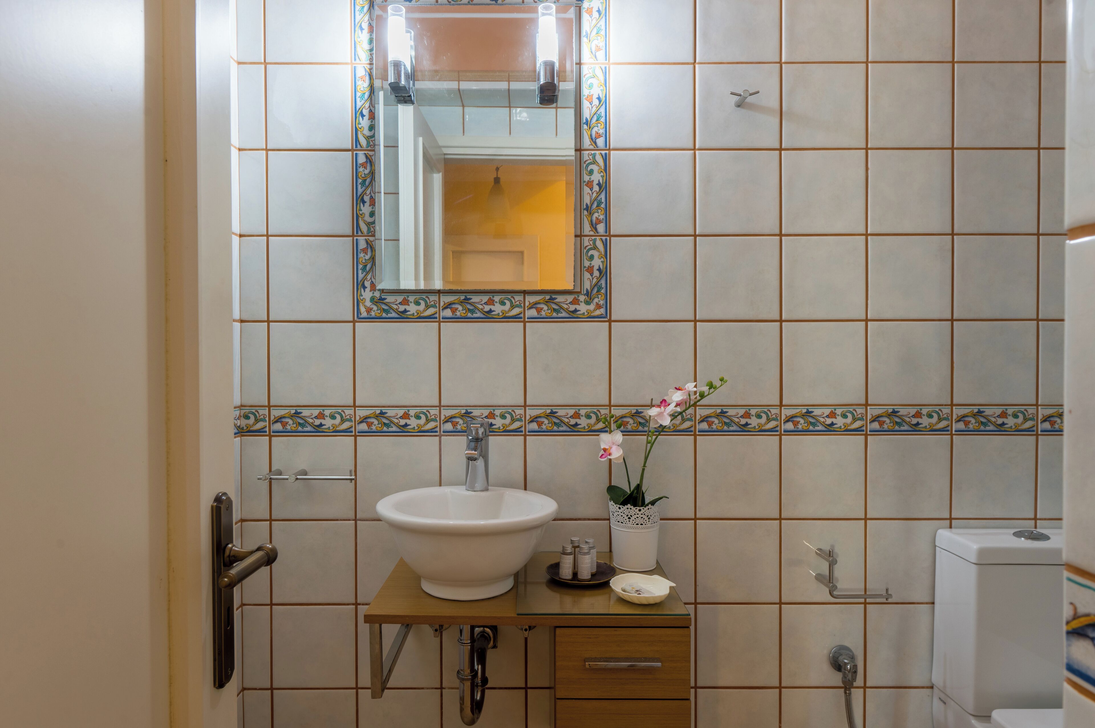 Une salle de bain avec un grand lavabo blanc, un miroir doté d’un cadre décoratif, une petite orchidée en pot et des toilettes.