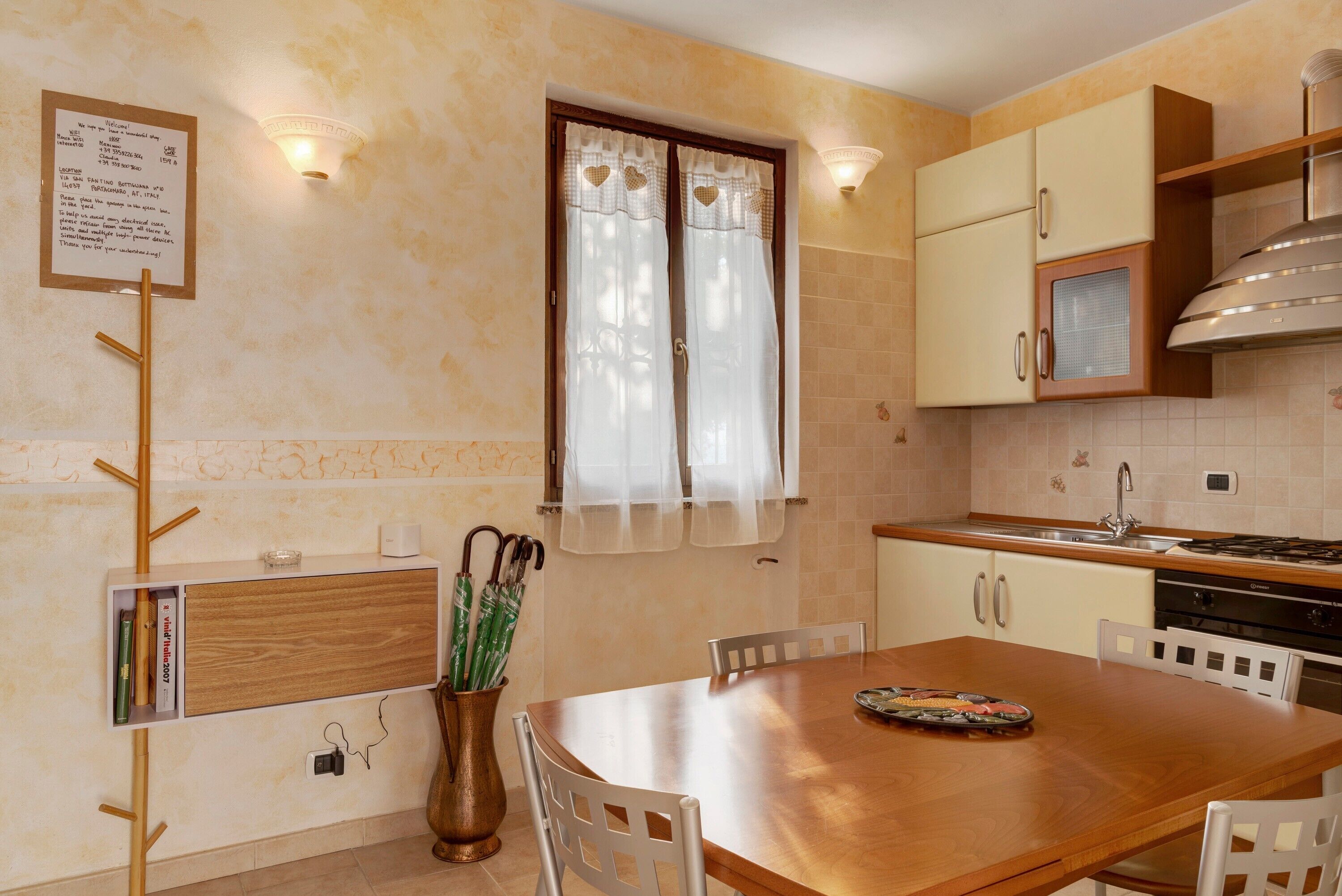 Uma cozinha com mesa de madeira, cadeiras, janela com cortinas e luminária na parede.