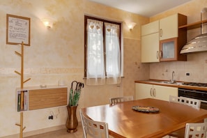 Une cuisine avec une table en bois, des chaises, une fenêtre avec des rideaux et un luminaire fixé au mur.