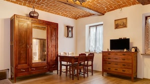 A room with a wooden cabinet, a dining table with chairs, a television, and a window with curtains. - Holiday Home 'Casa Dello Zio' with Mountain View, Wi-Fi and Air Conditioning (Portacomaro)