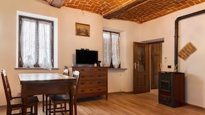 A room with a wooden dining table, chairs, a television, a fireplace, and a window with curtains. - Holiday Home 'Casa Dello Zio' with Mountain View, Wi-Fi and Air Conditioning (Portacomaro)