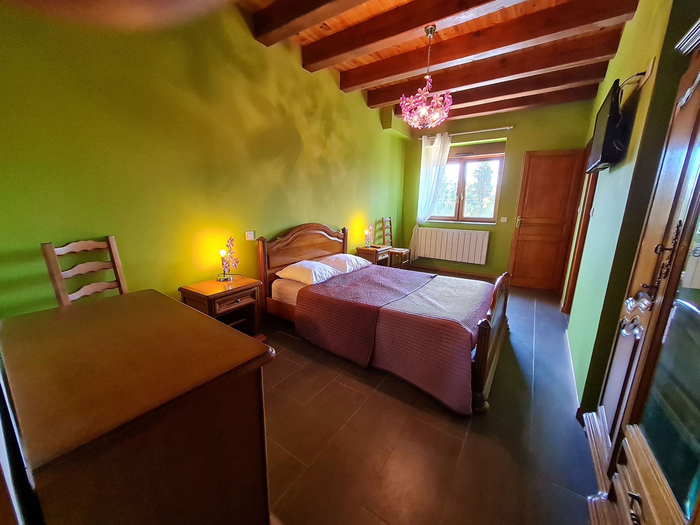 Une chambre à coucher avec un lit en bois, une table de chevet, une chaise et une fenêtre avec des rideaux.