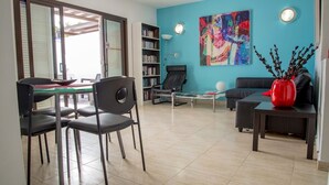 Ein modernes Wohnzimmer mit Essbereich, Bücherregal, einem farbenfrohen abstrakten Gemälde und einer roten Vase auf einem Beistelltisch.