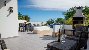 Eine Terrasse im Freien mit Korbmöbeln, einem Grill und einem Pool im Hintergrund.