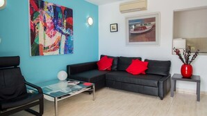 Ein modernes Wohnzimmer mit einer schwarzen Couch, roten Kissen, einem Glastisch und einem farbenfrohen abstrakten Gemälde an der Wand.