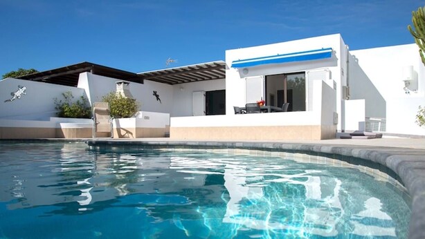 Ein moderner Poolbereich mit einem klaren, blauen Pool, einem weißen Gebäude mit blauen Akzenten und einer Pergola.