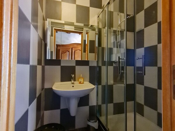 A bathroom with a checkered tile pattern, a white sink with a mirror above it, and a glass shower enclosure. - Cozy B&B near Luxembourg and Belgium (Xivry-Circourt)