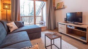 A modern living room with a sofa, a coffee table, a TV, and a wooden cabinet. - Valmorel: Apt for 6, 2 bdrm, parking, wifi, ski-in/ski-out (Valmorel)