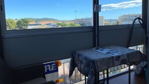 A room with a large window, a table with a floral tablecloth, and a view of buildings and trees.