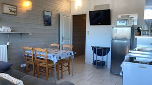 A compact living space with a dining area, a sofa, a kitchen with a refrigerator and microwave, and a TV mounted on the wall.