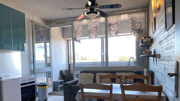 A compact kitchen with a dining area, a ceiling fan, and a window with curtains.