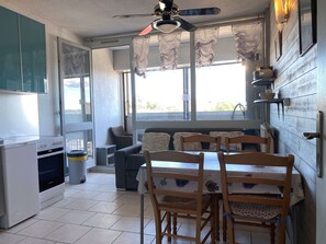 Une cuisine de taille réduite avec un coin repas, un ventilateur de plafond et une fenêtre avec des rideaux.