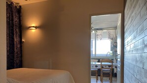 A bedroom with a bed, a bathroom with a shower curtain, and a view into a dining area with a table and chairs.