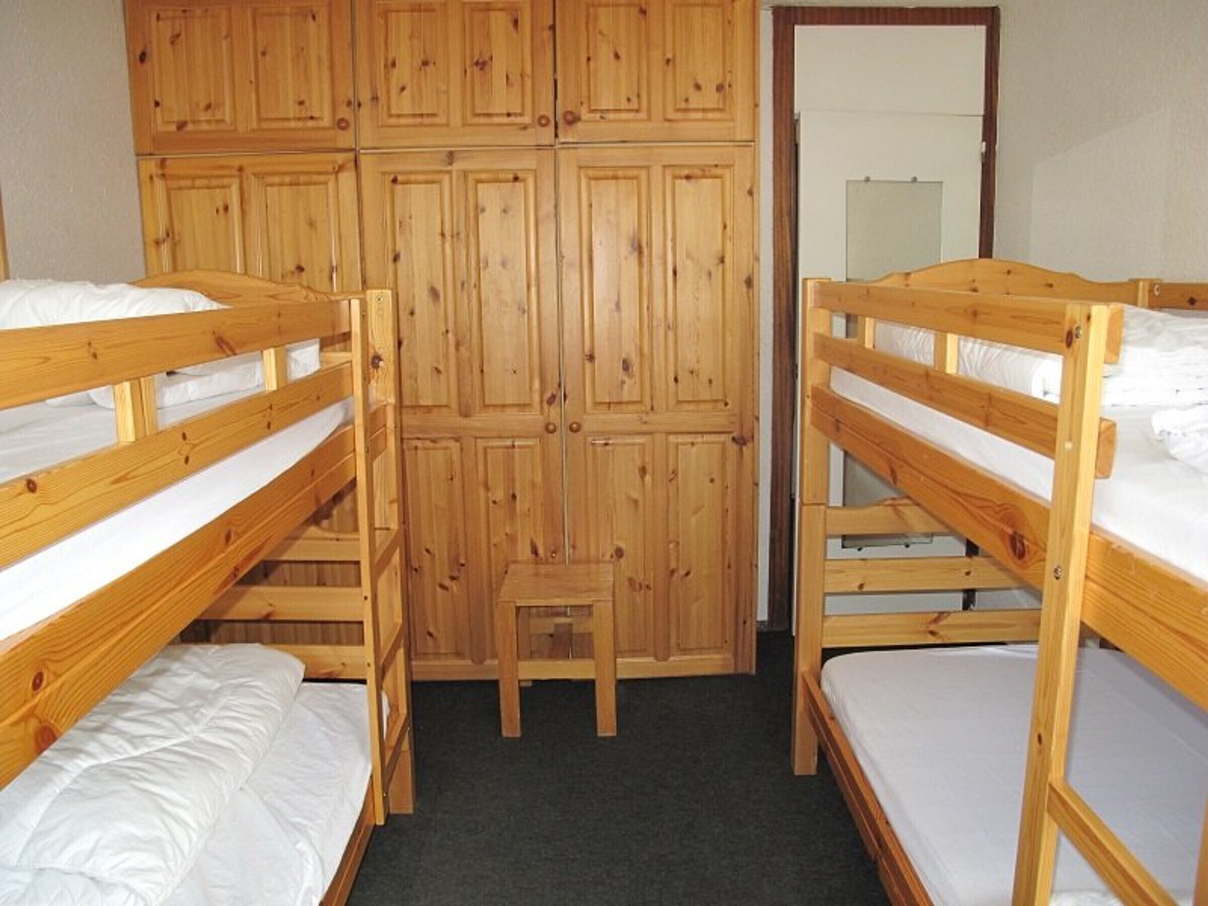A room with two bunk beds, a wooden wardrobe, and a small wooden stool.