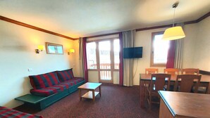 A furnished living room with a sofa, a small table, a dining table with chairs, a television, and a window with curtains. - 3-room apartment, ski-in/ski-out, sleeps 7, Plagne Soleil (Plagne Soleil)