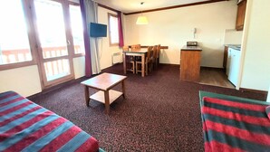 A compact room with two single beds, a small table, a chair, a TV, a dining table with chairs, a kitchen area, and large windows with curtains. - 3-room apartment, ski-in/ski-out, sleeps 7, Plagne Soleil (Plagne Soleil)