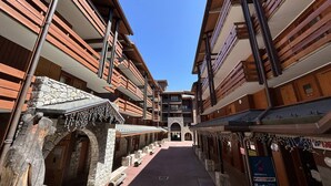 Una calle estrecha bordeada por edificios de varios pisos con balcones, muros de piedra y un cielo azul despejado.
