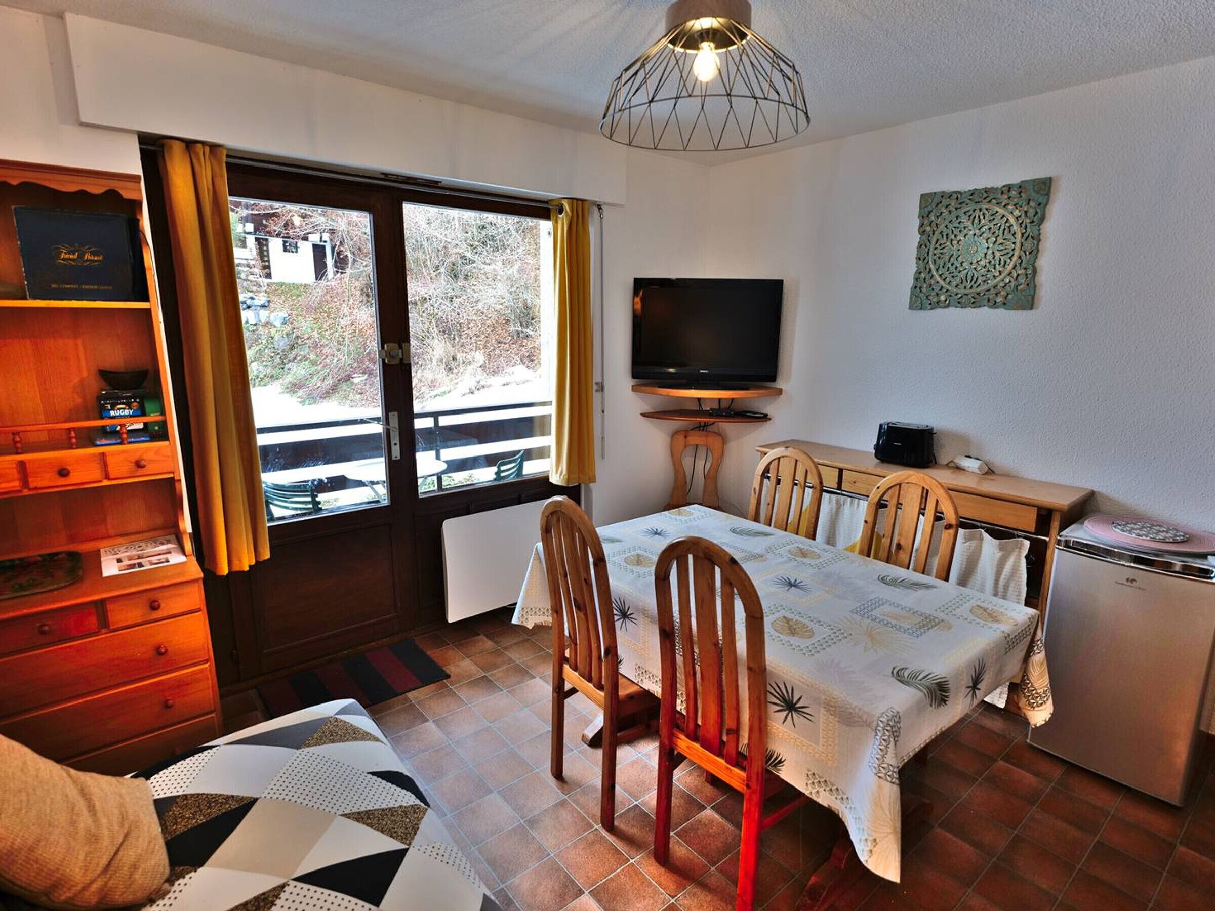 A cozy room with a dining table, chairs, a television, and a small kitchenette.