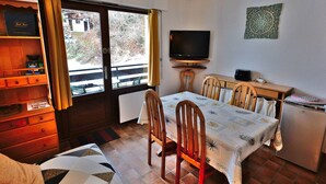 A cozy room with a dining table, chairs, a television, and a small kitchenette.