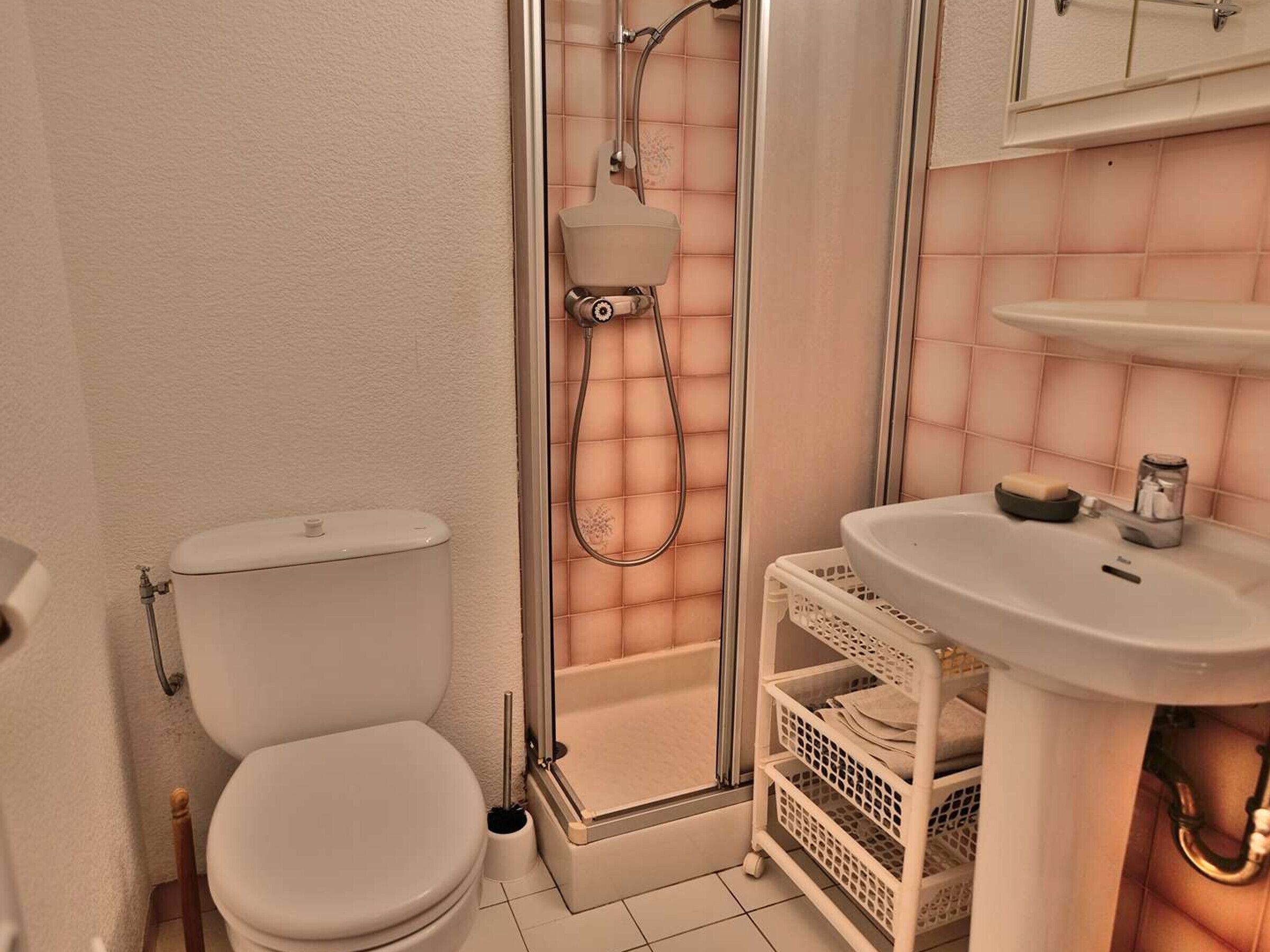 A bathroom with a toilet, a shower enclosure, a sink, and a storage basket.