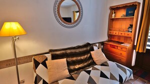 A room with a sofa, a lamp, a mirror, and a wooden cabinet with shelves.