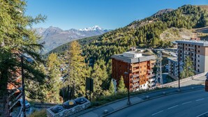 A modern building with a stone base and wooden upper floors, surrounded by a mountainous landscape with a clear sky. - 2-room apartment with balcony and garage, 100m from slopes (La Plagne-Tarentaise)