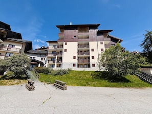 A multi-story hotel with balconies, a stone facade, and a grassy area with a bench. - 2-Room Duplex for 6 in Vallandry - Pets Allowed (Peisey-Vallandry)