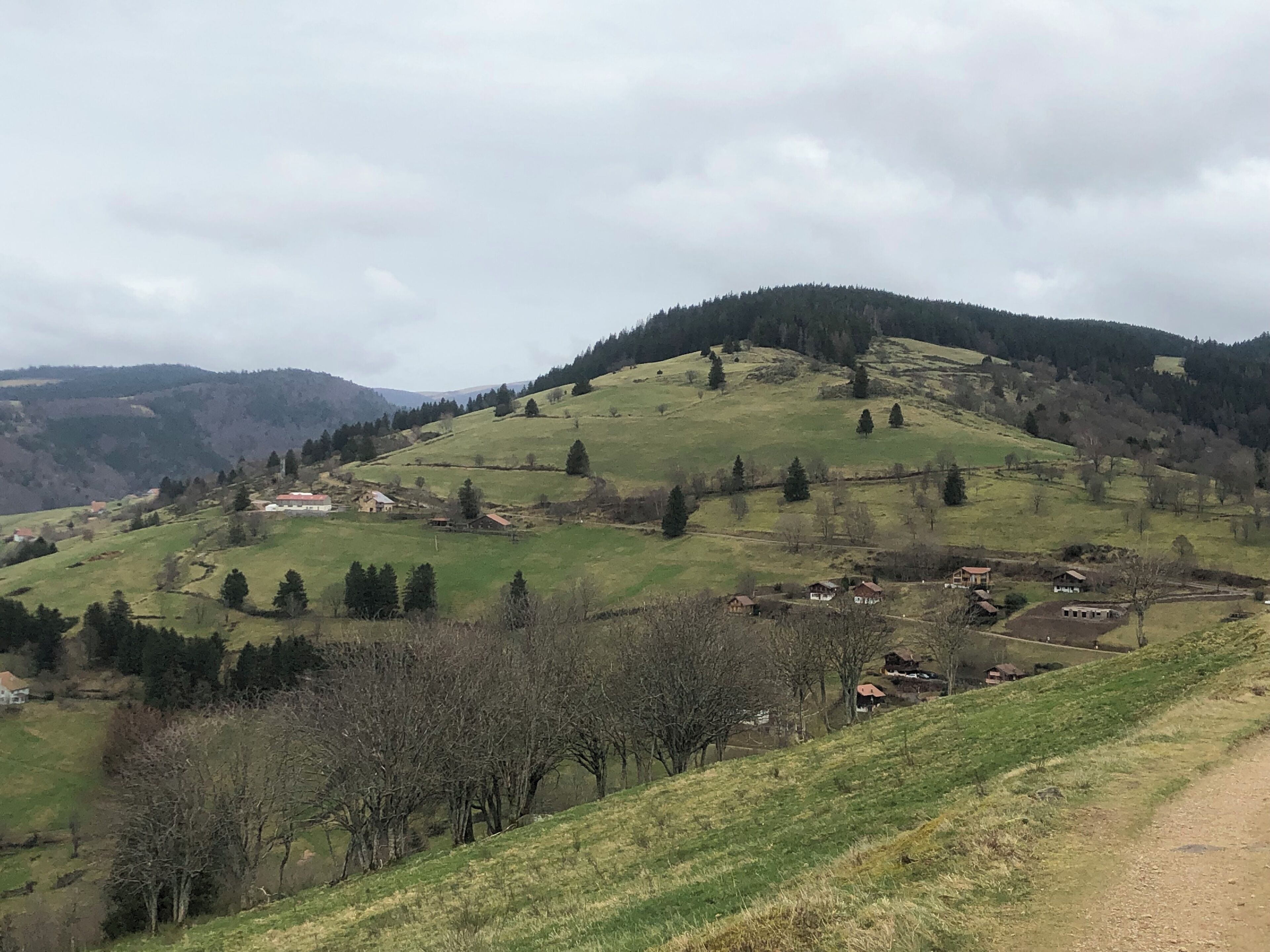 A rural landscape with rolling hills, scattered houses, and a dirt road.