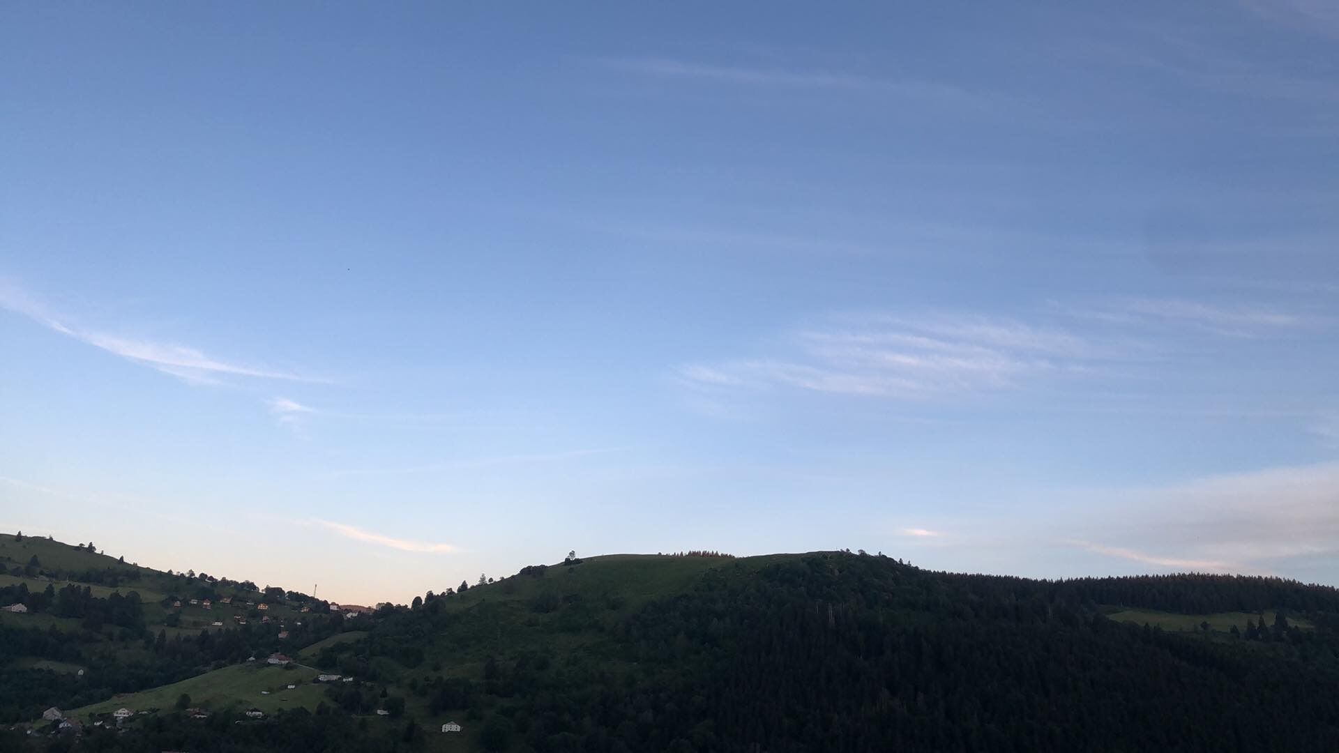 A panoramic view of a hilly landscape with scattered houses and dense forest areas.