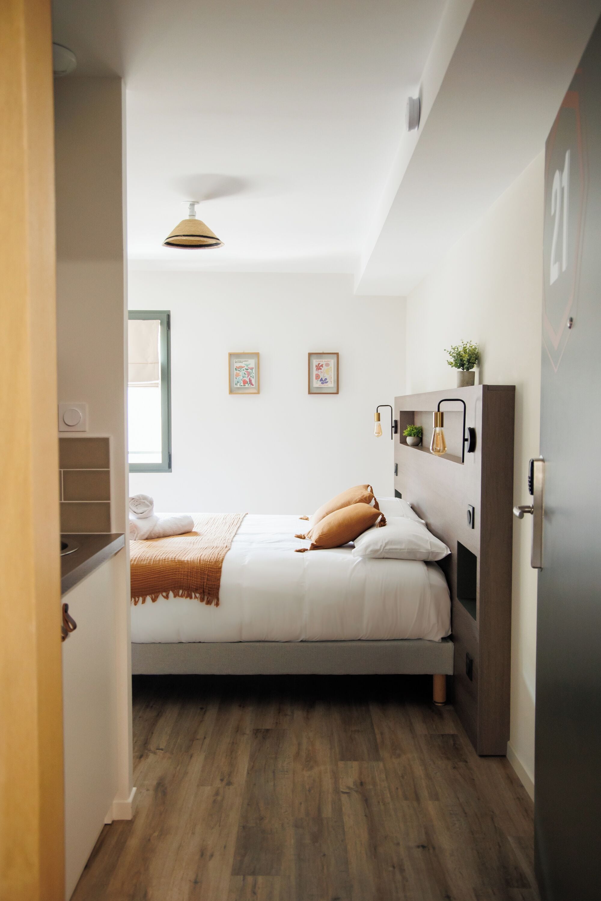 A bedroom with a bed, a bedside table, a wall-mounted shelf with decorative items, a ceiling fan, and a window.
