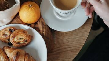 Una mesa de madera con un plato de cruasanes, una taza de café y una naranja.