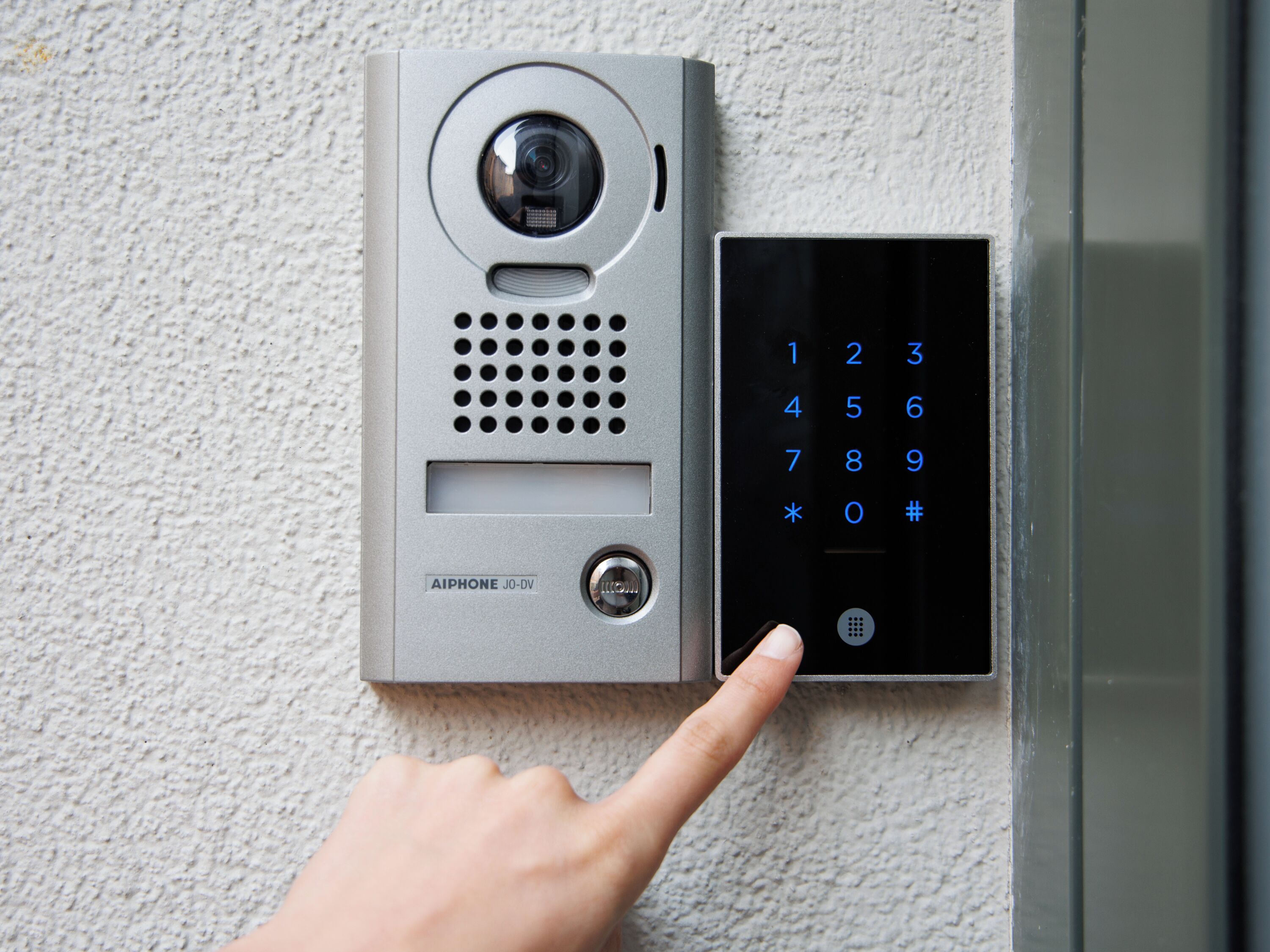 A wall-mounted intercom system with a numeric keypad and a camera.
