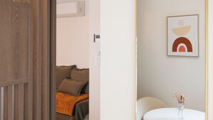 Ένα δωμάτιο με μια ξύλινη πόρτα, έναν στρογγυλό καθρέφτη, ένα στρογγυλό τραπέζι και ένα κρεβάτι με μια κουβέρτα.